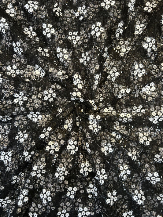 Close-up of shimmering black net textile with all-over white sequin flower patterns, ideal for festive party wear suits and anarkalis.