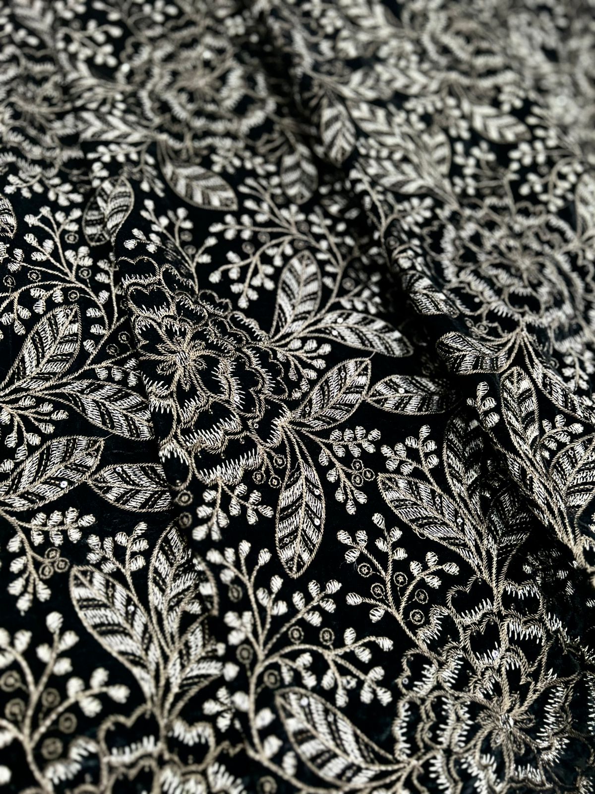 New style premium black velvet fabric with intricate gold and silver zari embroidery in a floral and leaf motif. Luxurious texture, high-quality micro eagle velvet, ideal for formal wear for men.
