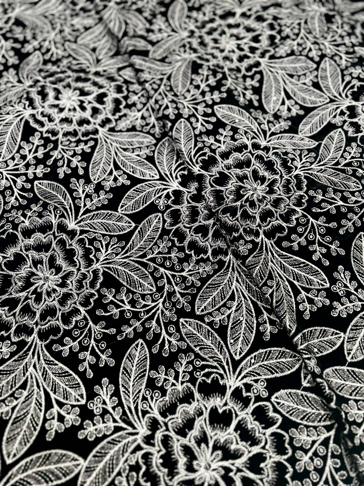  This gorgeous premium black velvet is covered in a lush, detailed design using sparkling silver and white thread. The floral and leafy pattern gives it a rich, sophisticated feel. Imagine the elegant outfits you could create with this new style fabric!"