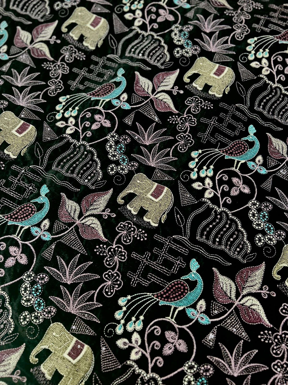  "Discover this enchanting premium velvet fabric featuring a delightful array of embroidered motifs! On a rich dark background, you'll find charming elephants, elegant peacocks, and intricate floral and leaf patterns in soft shades of cream, blue, and purple. It's truly a work of art!"
